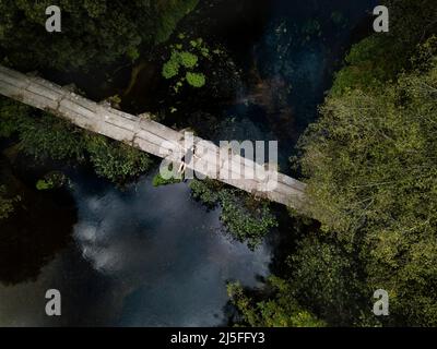 Luftaufnahme einer Frau, die auf einer alten Steinbrücke über den Fluss Umia in As Aceñas liegt Stockfoto