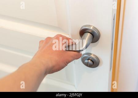 Die Hand drückt den Türknopf einer weißen Tür Stockfoto