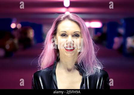 Nahaufnahme eines lächelnden, schönen jungen Mannes mit rosa Haaren und schwarzer Lederjacke in der beleuchteten Parkgarage Stockfoto