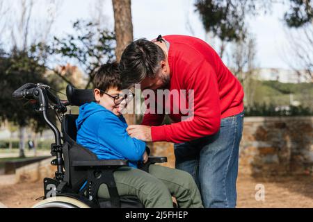 Vater spielt mit seinem Sohn mit Behinderung im Rollstuhl, während sie gemeinsam im Park Zeit genießen. Stockfoto