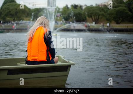 Ein Mädchen auf einem Grundstück auf einem Boot. Frauen in einer orangefarbenen Wasserschutzweste. Ein Mann im Park booten. Stockfoto