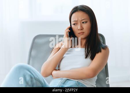 Verwirrt aufgeregt gebräunt schöne junge asiatische Frau hören schockiert Nachrichten beim Anruf mit Telefon zu Hause innen Wohnzimmer. Fernkommunikation Social Stockfoto