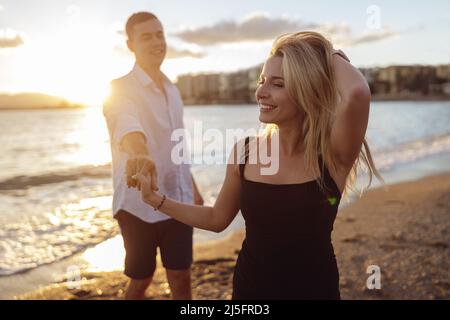 Lächelnde Dame in schwarzem Kleid, die mit einem Mann am Meer steht Stockfoto
