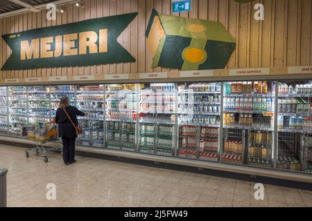 Schöne Innenansicht eines ICA Supermarkts. Frau, die Milchprodukte aus Kühlschränken im Supermarkt kauft. Schweden. Stockfoto
