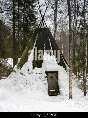 Ein traditionelles sami-Zelt (kota), bedeckt mit einem moosigen Stoff, in einem verschneiten finnischen Tannenwald Stockfoto