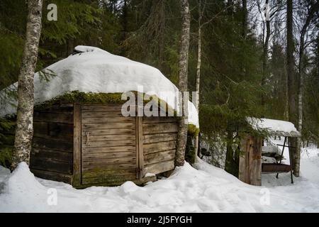 Rovaniemi, Finnland - 18.. März 2022: Ein Holzschuppen in einem verschneiten Tannenwald in Finnland. Stockfoto