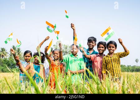 Gruppe von Dorf Teenager-Kinder winken indische Flagge durch Blick auf Kamera auf Paddy abgelegt - Konzept der Unabhängigkeit oder republic Day Feier, Freiheit Stockfoto