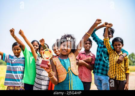 Fröhliche Teenager-Mädchen feiern, indem sie Trophäe vor ihrer Unterstützung Blick auf die Kamera halten - Konzept der Leistung, Freundschaft und erfolgreich. Stockfoto