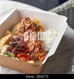 Fast Food Delivery. Griechische Souvlaki, Salat und Gyros Take-Away-Menü aus Fastfood-Restaurant serviert in recycelbaren Pappteller auf dem Tisch. Stockfoto