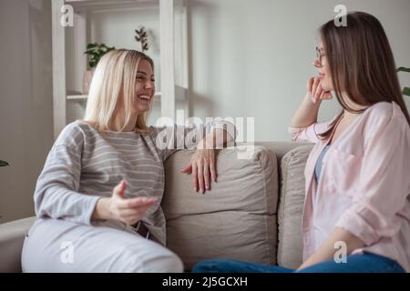 Junge Freundinnen reden, lächeln zusammen, sitzen zu Hause auf dem Sofa Stockfoto