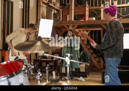 Ein Mädchen singt in ein Mikrofon, zwei Jungs spielen eine E-Gitarre. Band probt eine Performance. Stockfoto