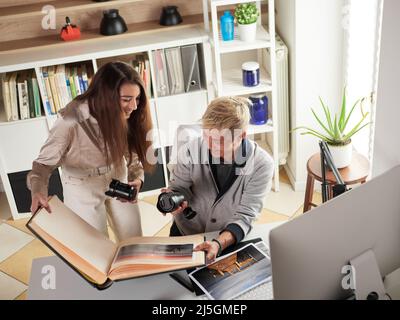 Fotografen, die am Arbeitsplatz mit zwei Computern im Studio mit einem Laptop arbeiten Stockfoto