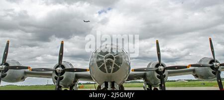 Vorderansicht eines B-29 Super Fortress Bombers aus dem Zweiten Weltkrieg mit einem Verkehrsflugzeug, das im Hintergrund in einem dramatischen Himmel abheben soll. Stockfoto