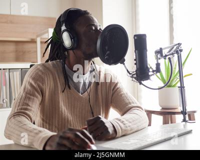 Afroamerican glücklich junge männliche Aufnahme Audio-Blog in Kopfhörer Mikrofon zu Hause senden ... Stockfoto