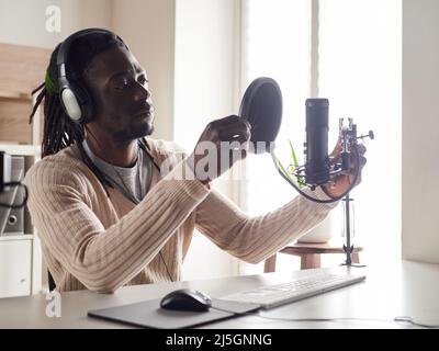 Afroamerican glücklich junge männliche Aufnahme Audio-Blog in Kopfhörer Mikrofon zu Hause senden ... Stockfoto