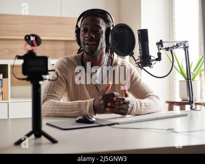 Afroamerican glücklich junge männliche Aufnahme Audio-Blog in Kopfhörer Mikrofon zu Hause senden ... Stockfoto