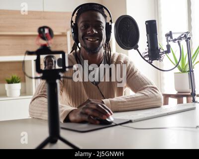 Afroamerican glücklich junge männliche Aufnahme Audio-Blog in Kopfhörer Mikrofon zu Hause senden ... Stockfoto