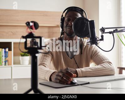 Afroamerican glücklich junge männliche Aufnahme Audio-Blog in Kopfhörer Mikrofon zu Hause senden ... Stockfoto