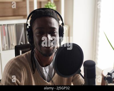 Afroamerican glücklich junge männliche Aufnahme Audio-Blog in Kopfhörer Mikrofon zu Hause senden ... Stockfoto