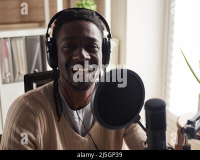 Afroamerican glücklich junge männliche Aufnahme Audio-Blog in Kopfhörer Mikrofon zu Hause senden ... Stockfoto