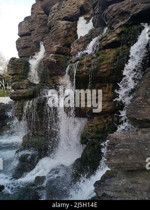 Blick auf einen ornamentalen Wasserfall mit mehreren Kaskaden, die über einer Felswand in einem Park in Paris fallen. Stockfoto