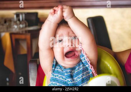 Ein kleines Kind wirft in einem Restaurant einen Wutanfall auf ihren Hochstuhl Stockfoto