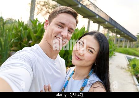 Lächelndes multirassisches Paar, das während des Sonnenuntergangs in einem Uran-Park ein Selfie gemacht hat Stockfoto