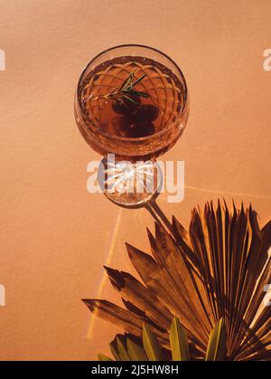 Weinspritzer oder Gin Tonic mit Trauben und Rosmarin-Zweig, ein leckerer Sommercocktail, isoliert auf beigem Boho-Hintergrund mit getrockneten Palmblättern Stockfoto
