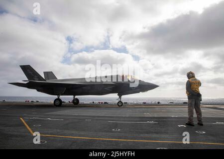 220411-N-IV962-2171 PAZIFISCHER OZEAN (11. April 2022) – Yuriy Dyshkant, der Partner des Chief Aviation Boatswain (Handling), leitet einen F-35B Lightning II, der dem Marine Fighter Attack Squadron (VMFA) 12aboard amphibischen Angriffsschiff USS Makin Island (LHD 8) zugewiesen wurde, 11. April. Piloten führen Qualifikationen zur Landung an Deck durch, um die Start- und Landungen an Bord zu üben. Makin Island ist ein amphibisches Angriffsschiff der Wasp-Klasse, das Routineoperationen in der US-Flotte von 3. durchführt. (USA Navy Foto von Mass Communication Specialist 3. Class Nadia Lund) Stockfoto