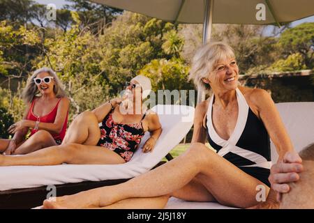 Glückliche ältere Freunde, die lachen und Spaß haben, während sie sich auf den Liegen entspannen. Gruppe älterer Menschen, die ihren Sommerurlaub in einem Kurort genießen. Senio Stockfoto