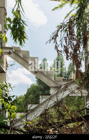 Weiße Eisentreppe oder weiße Stahltreppe, weiße Metalltreppe zwischen den Ruinen in verlassenen Gebäude wurde im Laufe der Zeit und sichtbar par verschlechtern links Stockfoto