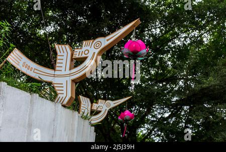 Zwei Holzvogelornamente mit hängenden roten Zierblumen, die unter einem Baum in einem Seepark in Hanoi hängen. Stockfoto
