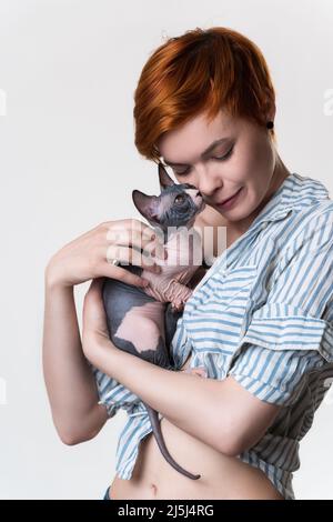 Rotschopf junge Frau mit geschlossenen Augen sanft umarmt Katze Blick auf Besitzer. Studio auf weißem Hintergrund aufgenommen. Portrait schöne Hipster mit kurzen Haaren Stockfoto