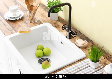 Frische grüne Äpfel im Waschbecken und verschiedene Geschirrtücher auf der Holztheke in der Nähe der Farbwand Stockfoto