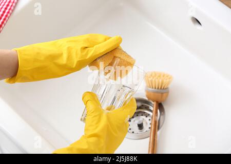 Frau in Gummihandschuhen, die Glas im Waschbecken waschen, Nahaufnahme Stockfoto