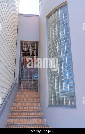 Eine Treppe mit Ziegelsteinen führt zu einem schmiedeeisernen Eingangstor in San Francisco, Kalifornien. Haus außen mit Treppe in der Mitte der beigen Wand auf der l Stockfoto
