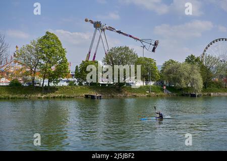 Stuttgart, Deutschland - 22. April 2022: Frühlingsfest mit lustigen Fahrgeschäften. Riesenrad und Unendlichschaukel am Fluss am Mittag. Deutschland, Stockfoto