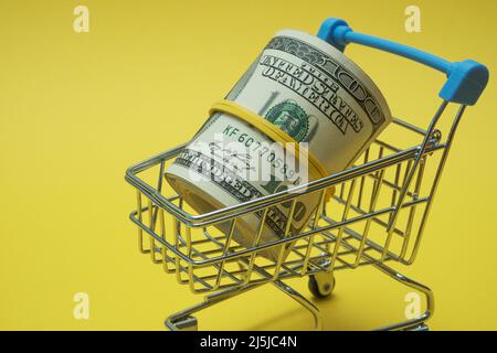 In einen Schlauch gerollte Dollars liegen in einem Einkaufskorb. Stockfoto