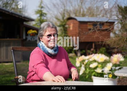 Kienitz, Deutschland. 12. April 2022. Barbara Brunat, Betreiberin des Erlenhofs, sitzt an einem Tisch im Garten. Von April bis Oktober bietet der Ferienhof im Mittleren Oderbruch naturnahe Ferien auf weitläufigen Gelände und Übernachtungen in sechs Hirtenwägen und in einer Blockhütte. Maximal 15 Gäste finden auf dem Bauernhof Platz zum Schlafen, und es gibt weder Fernseher noch Radios in den Waggons und in der Kabine. (To dpa: ' 'Schäferstündchen im Schäferwagen' im Oderbruch') Quelle: Soeren Sache/dpa/Alamy Live News Stockfoto