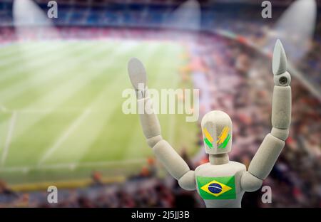 Hölzerne Schaufensterpuppe mit den Farben der brasilianischen Mannschaft feiert mit einem Fußballstadion im Hintergrund Stockfoto