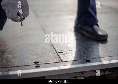 Der Arbeiter hält den Bolzen fest. Mann zieht Schraube an. Guy baut die Struktur zusammen. Passend zur Bohrung. Die Person sucht nach einem Loch in der Platine. Stockfoto