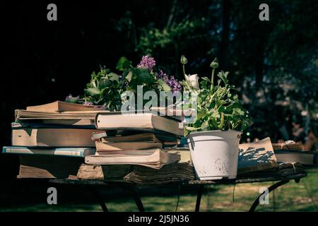 Stapel antiker Bücher auf einem schmiedeeisernen Tisch in einem Garten. Stockfoto