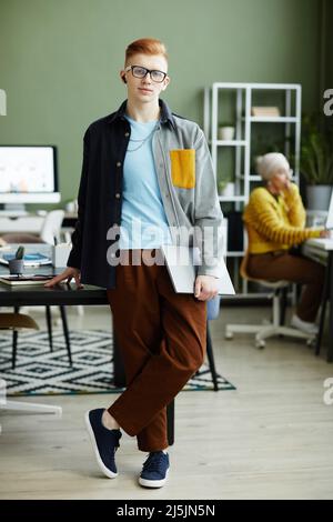 Porträt eines jungen Mannes mit rothaarigen Haaren in lebendigem Stil und einem Lächeln auf die Kamera, während er im Büro steht Stockfoto