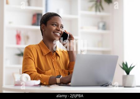 Geschäftsfrau, die mit einem Laptop am Tisch sitzt und telefoniert Stockfoto