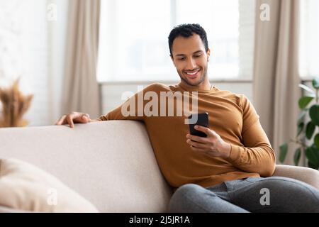 Glücklicher arabischer Mann, der Mobiltelefon mit kabellosen Kopfhörern benutzt Stockfoto