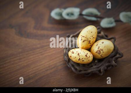 Schokoladennest, schokoladengoldene Eier und Weidenzweig auf dunklem Holzhintergrund Stockfoto