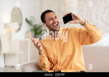 Verspielter arabischer Mann mit Mobiltelefon, Kopfhörer und Gesang Stockfoto