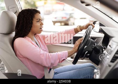 Wütende schwarze Frau, die Auto fährt, schreit und hupt Stockfoto