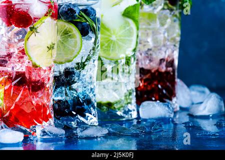 Kalte Sommercocktails Getränke. Klassischer alkoholischer Longdrink und Mojito oder Mocktail in Highballs mit Heidelbeeren, Brombeeren, Himbeeren, Limette, Kraut Stockfoto