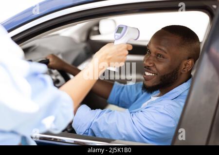 Medizinischer Arbeiter, Der Die Körpertemperatur Des Black Man Driving Car Überprüft Stockfoto